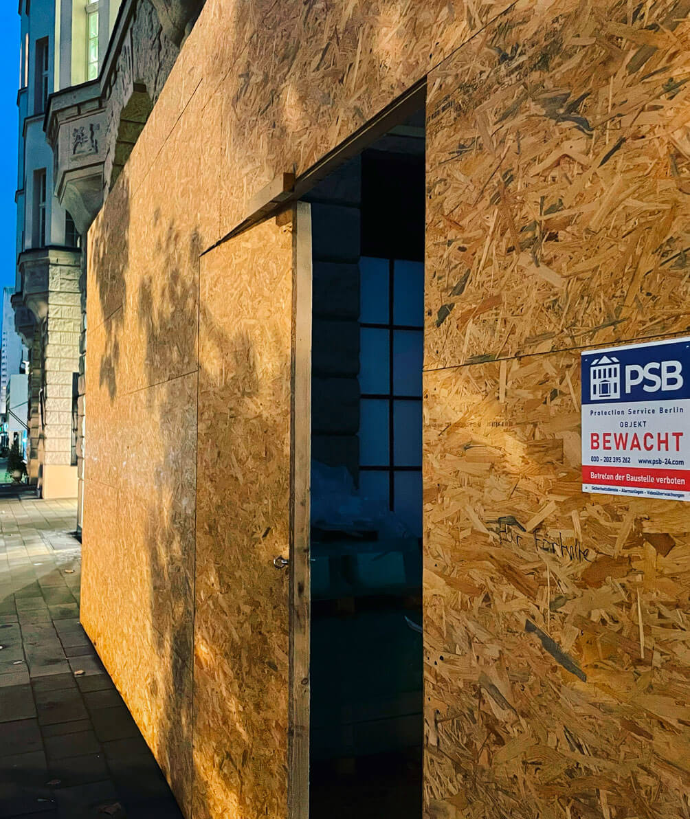 mit Holzplatten abgeschirmte Gebäudefassade mit der Markierung "Bewacht durch PSB"